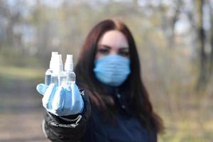 giovane donna nel protettivo maschera Spettacoli disinfettante spray bottiglie all'aperto nel primavera legna foto