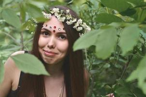 un' foresta immagine di un' bellissimo giovane brunetta di europeo aspetto con buio Marrone occhi e grande labbra. su il ragazze testa è indossare un' floreale ghirlanda, su sua fronte brillante decorazioni foto