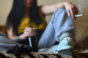 un' ragazza seduta su il divano, fumo un' sigaretta, potabile birra foto