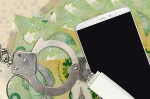 20 canadese dollari fatture e smartphone con polizia manette. concetto di gli hacker phishing attacchi, illegale truffa o il malware morbido distribuzione foto