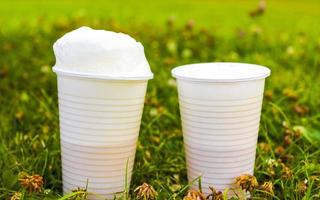 bianca plastica tazze con birra e schiuma corona su erba. foto