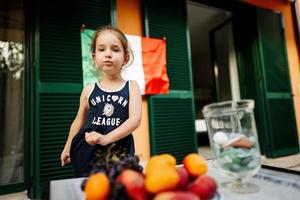 contento bambino ragazza contro italiano bandiera festeggiare repubblica giorno di Italia e mangiare frutta. foto