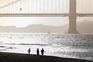 persone a piedi su il spiaggia con il d'oro cancello ponte dietro. foto