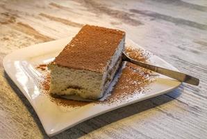 Tiramisù torta nel un' bianca piatto su il tavolo con cucchiaio. foto