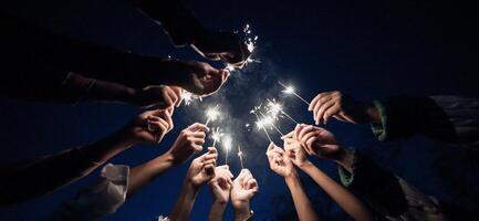 gruppo di giovane amici godere con ardente sparkler nel mani insieme foto