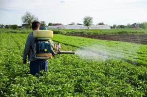 un' contadino spray sostanze chimiche su un' Patata piantagione campo. è aumentato raccolto. controllo di uso di sostanze chimiche in crescita cibo. protezione di coltivato impianti a partire dal insetti e fungine infezioni. foto