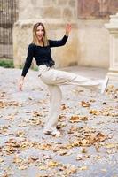 allegro giovane donna calciando caduto le foglie mentre a piedi nel parco foto