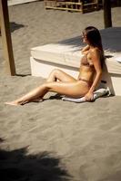 giovane donna nel bikini seduta su il spiaggia a estate giorno foto
