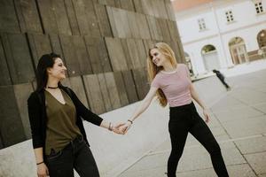 Due giovane donne a piedi su il strada e Tenere mani foto