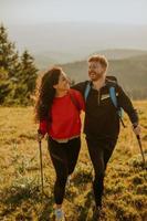 coppia sorridente che cammina con zaini su verdi colline foto