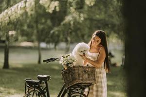 giovane donna con cane bianco bichon frise nel cestino della bici elettrica foto