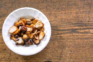 fresco shiitake fungo agitare fritte con soia salsa nel Cinese stile su bianca ceramica piatto e di legno sfondo. un' vegetariano cibo nel Cinese vegetariano Festival. foto