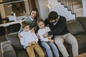 contento famiglia con Due bambini godere tempo insieme su divano nel vivente camera foto