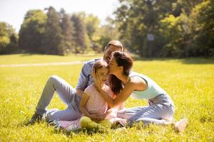 giovane famiglia felice con la piccola figlia carina che si diverte nel parco in una giornata di sole foto