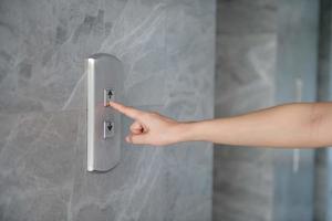 ritagliata mano di donna urgente spingere pulsante per ascensore su parete foto