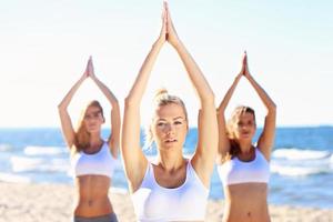 gruppo di donne praticando yoga su il spiaggia foto