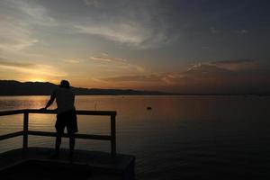 silhouette di un' giovane uomo in piedi di il lago godendo il tramonto. tranquillo, calmo atmosfera nel natura foto