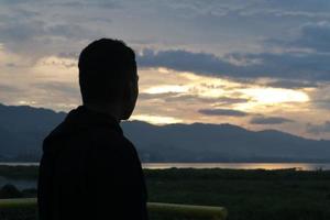 silhouette di un' giovane uomo in piedi di il lago godendo il tramonto. tranquillo, calmo atmosfera nel natura foto