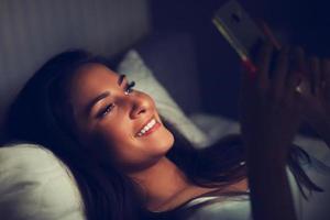 giovane bellissimo donna riposo nel letto con smartphone foto