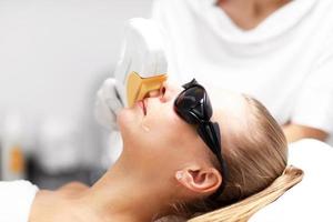estetista dando depilazione laser trattamento per donna su viso foto