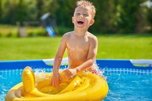 carino ragazzo nuoto e giocando nel un' Giardino dietro la casa piscina foto