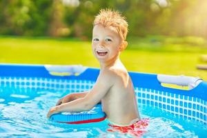 carino ragazzo nuoto e giocando nel un' Giardino dietro la casa piscina foto