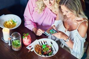 Due ragazza amici mangiare pranzo nel ristorante e utilizzando smartphone foto