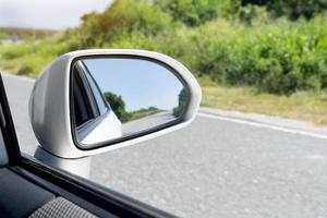 specchio Visualizza di bianca auto viaggio su il asfalto strada. con sfocato di verde erba a giorno. foto