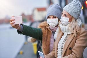 Due donne utilizzando smartphone e indossare maschere nel il città foto