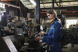 un industriale lavoratore nel protettivo e sicurezza uniforme e elmetto protettivo, giovane caucasico femmina ingegnere lavori con metallo macchina nel produzione fabbrica. professionale produzione meccanico occupazione. foto