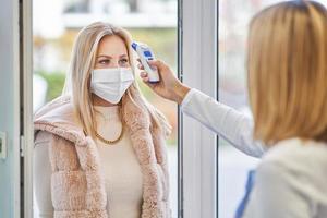 adulto donna nel medico maschera essere verificato per temperatura nel drogheria memorizzare foto