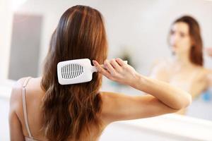 giovane donna in piedi nel bagno e spazzolatura capelli foto