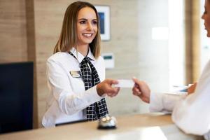 addetto alla reception dando chiave carta per donna d'affari a Hotel davanti scrivania foto