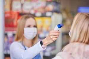 adulto donna nel medico maschera essere verificato per temperatura nel drogheria memorizzare foto