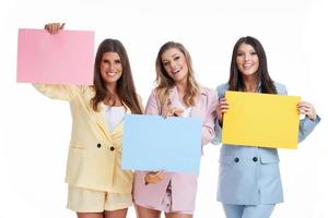 tre donne nel pastello tute Tenere tabellone in posa al di sopra di bianca sfondo foto