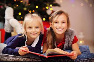 Due carino poco sorelle lettura storia libro insieme sotto Natale albero foto