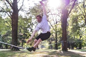 giovane uomo equilibratura e salto su slackline. uomo a passeggio, salto e equilibratura su corda nel parco. foto