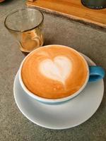 tazza di caldo cappucino è su il di legno tavolo. esso è un arte su il latte macchiato. foto