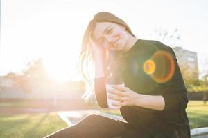 ritratto di giovane contento donna con lungo capelli con carta tazza di caffè nel città parco su d'oro ora foto