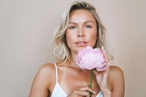 bellezza ritratto di bionda capelli sorridente giovane donna con rosa peonia nel mano isolato su bianca sfondo foto