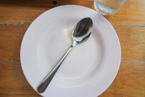 un vuoto bianca piatto con un' cucchiaio è posto su un' di legno tavolo. foto