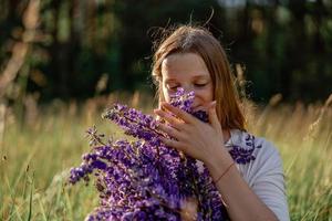 vicino su ritratto di giovane bellissimo testa Rossa donna con lentiggini, indossare bianca vestire, in posa nel il natura. ragazza con rosso capelli Tenere fiori. naturale bellezza. diversità, individuale unicità. foto