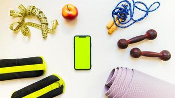 gli sport fitness concetti con Palestra attrezzatura. piatto posare di mobile Telefono con e sport attrezzatura su bianca tavolo sfondo. peso controllo, salutare stile di vita attrezzatura foto