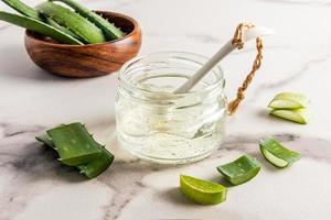 cosmetico bicchiere vaso con aloe Vera gel su un' bianca marmo tavolo e pianta fette. addizionale cura per problema pelle di il viso. foto