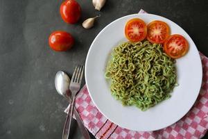 verde tagliatelle, o spinaci pasta , zucchine crudo vegano pasta immersione, e pomodori su piatto. foto