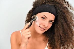 bellissimo giovane donna è lavaggio sua viso con viso spazzola foto