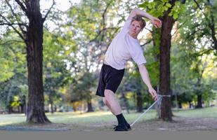 giovane uomo equilibratura e salto su slackline. uomo a passeggio, salto e equilibratura su corda nel parco. foto