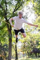 giovane uomo equilibratura e salto su slackline. uomo a passeggio, salto e equilibratura su corda nel parco. foto