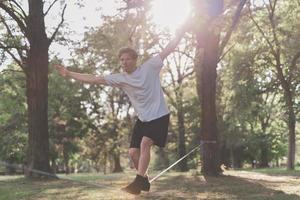 giovane uomo equilibratura e salto su slackline. uomo a passeggio, salto e equilibratura su corda nel parco. foto