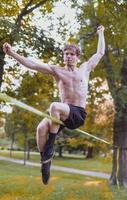 giovane uomo equilibratura e salto su slackline. uomo a passeggio, salto e equilibratura su corda nel parco. foto